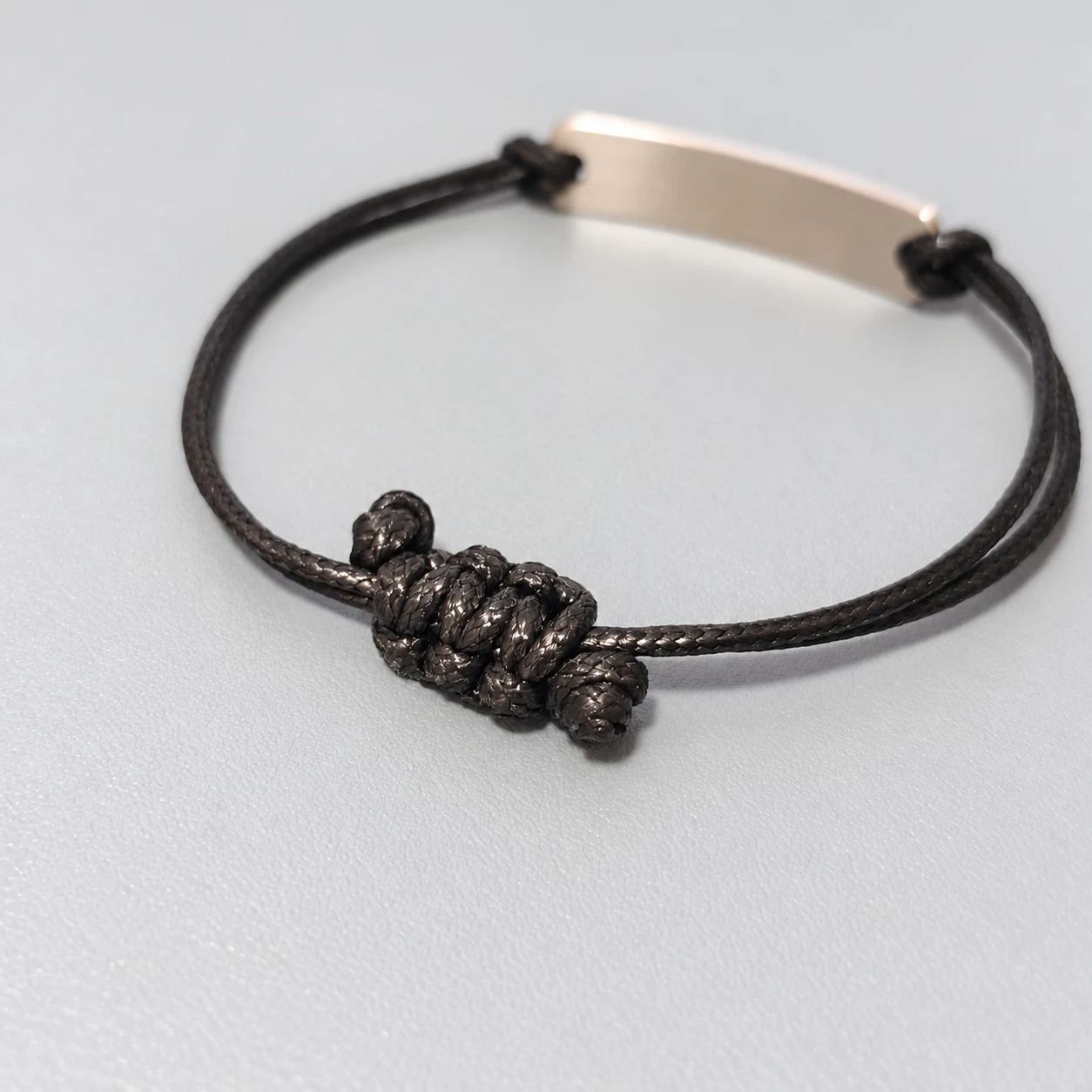 AI-assisted retouch of a real black cord bracelet sample showing the rear knot and reverse of the metal bar