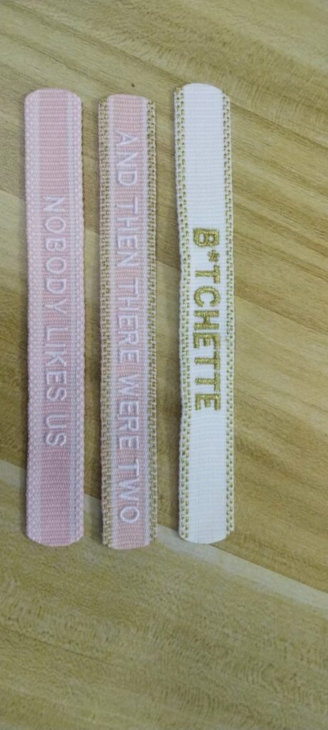 Actual pink and light-colored woven message band samples with white and gold-tone lettering